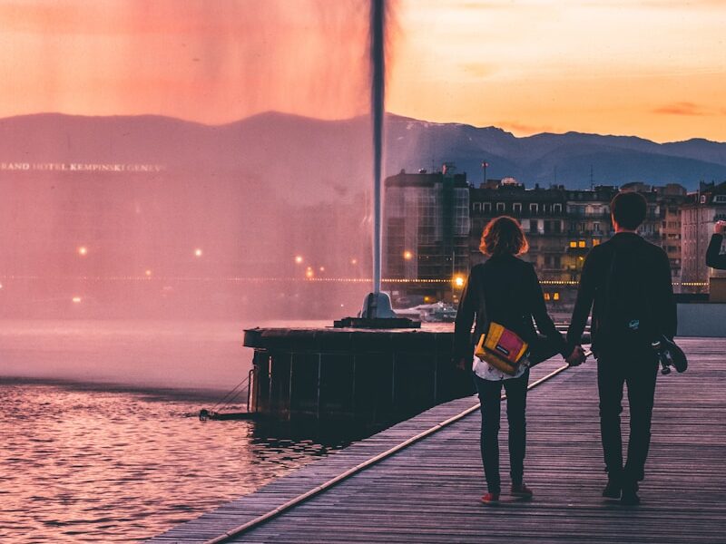 couple walking on wooden bridge near body of water