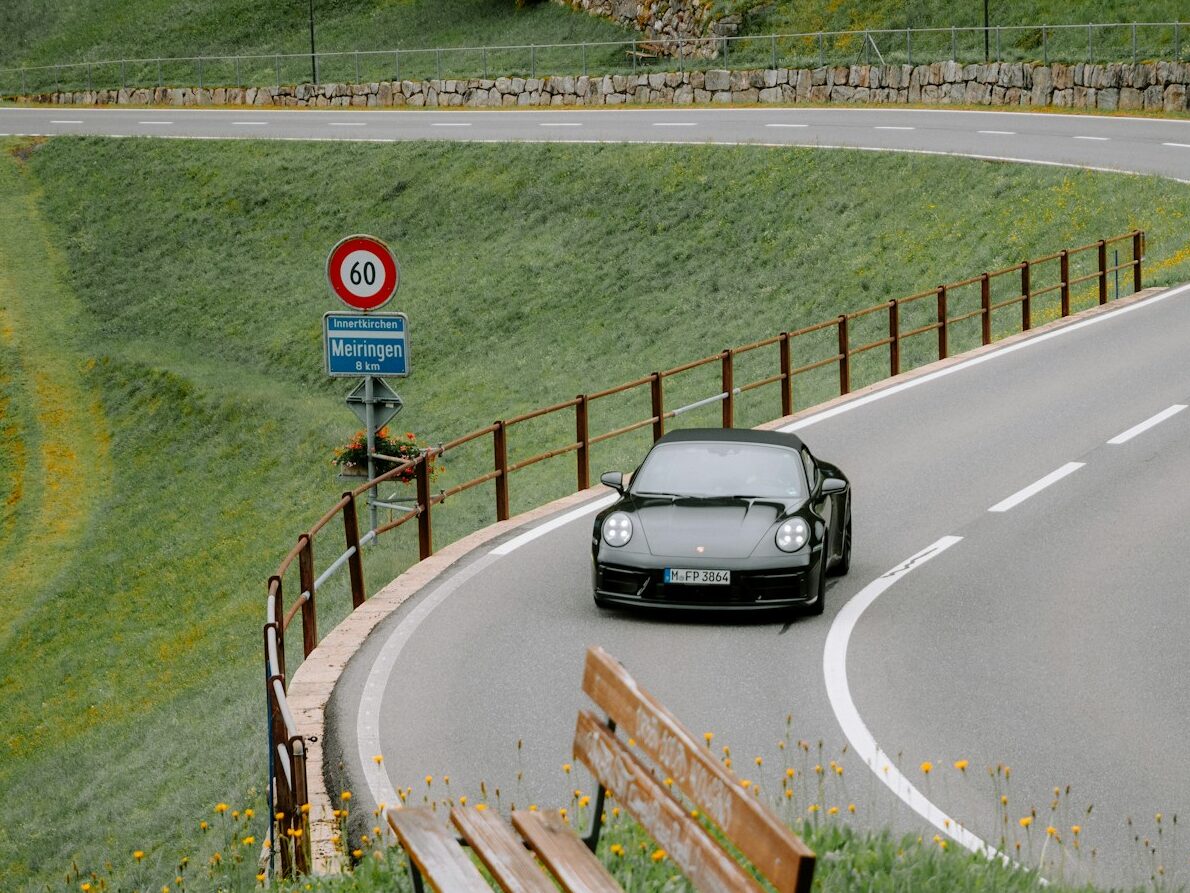 A car driving down a curvy road next to a wooden bench